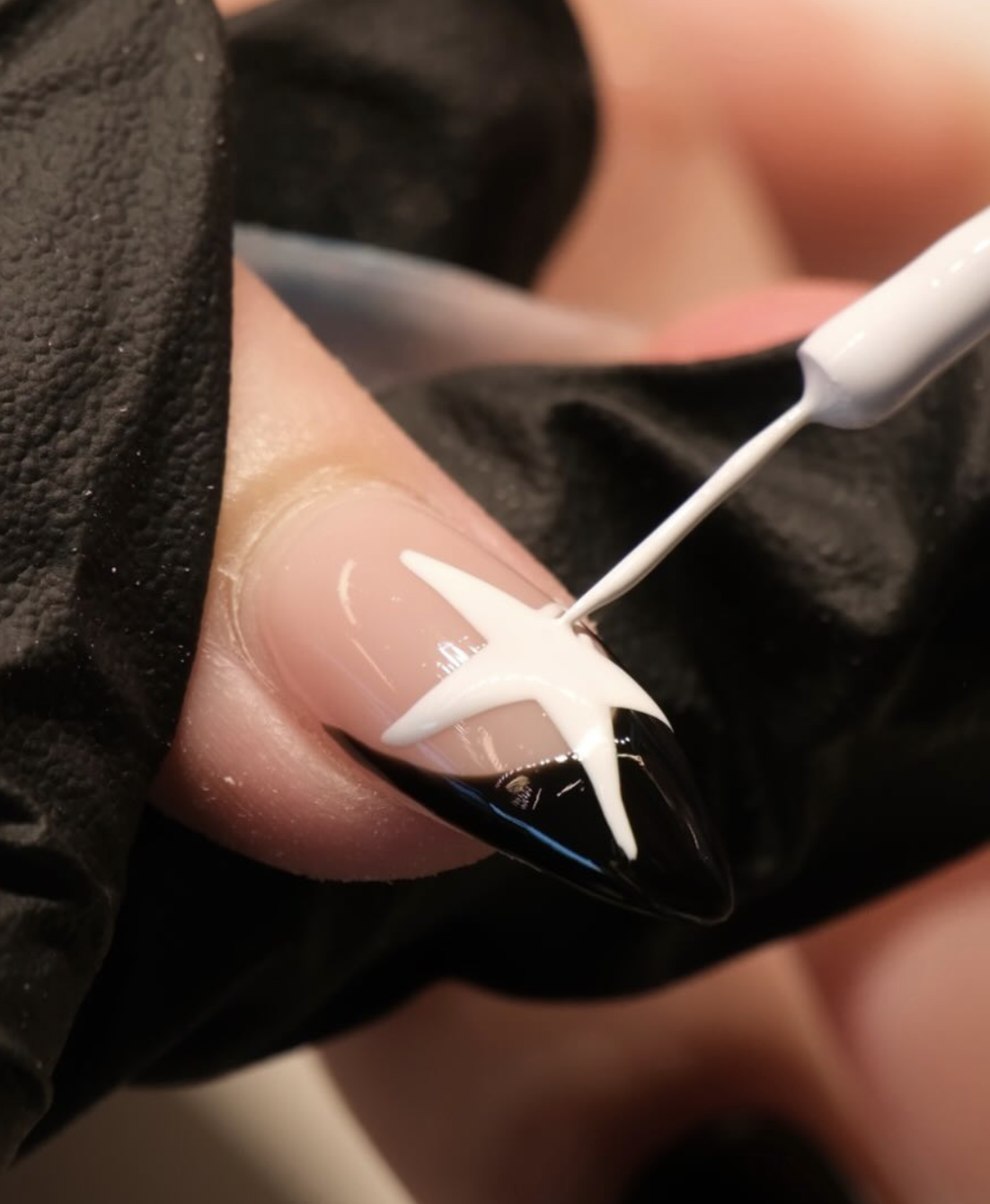 Nail artist painting white star nail art over a black French tip manicure at LUX Beauty Bar in Hamilton.